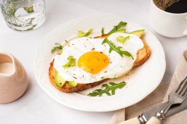 Hafif arka planda kızarmış yumurta, avokado ve roka ile nefis sandviç.