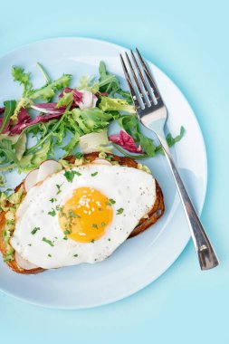 Lezzetli sandviç, kızarmış yumurta ve mavi arka planda salata.