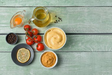 Lezzetli mayonez soslu kase ve yeşil ahşap arka planda malzemeler.