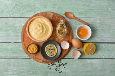 Lezzetli mayonez soslu kase ve yeşil ahşap arka planda malzemeler.