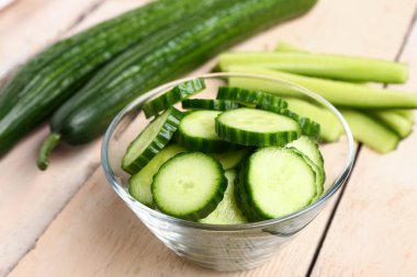 Hafif ahşap arka planda taze kesilmiş salatalıklı kase, yakın plan.