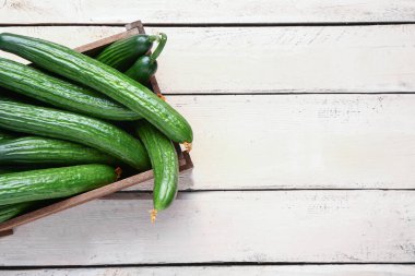 Hafif ahşap arka planda taze salatalıklı kutu, yakın plan.