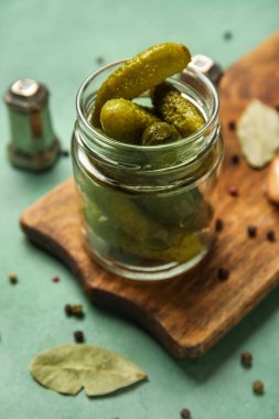 Lezzetli mayalanmış salatalıklı kavanoz ve yeşil arka planda tahta tahta.