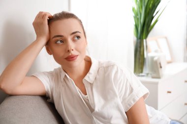 Evdeki koltukta oturan düşünceli genç bayan, yakın plan.