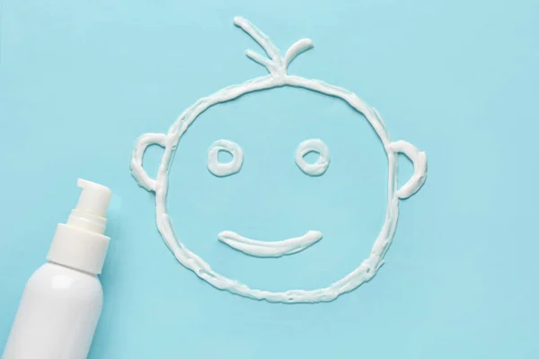 Drawing of baby face made with sunscreen cream on blue background