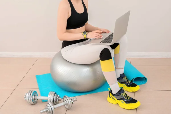 Sporty woman using laptop on fitball in gym