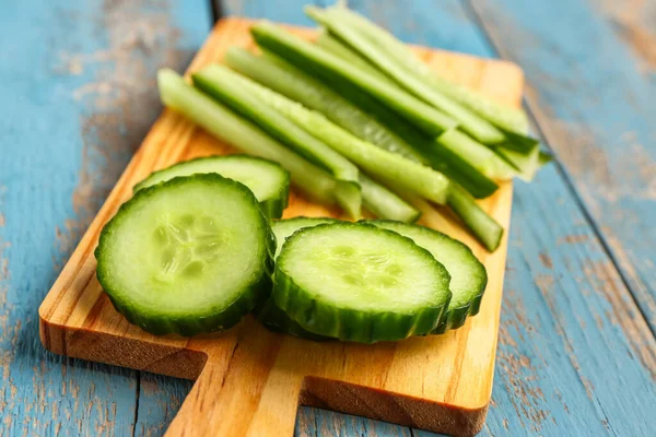 Board with fresh cut cucumber on blue wooden background, closeup