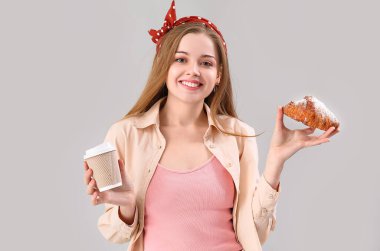 Young woman with tasty croissant and cup of coffee on grey background