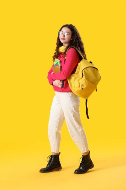 Female student with headphones, notebooks and backpack on yellow background