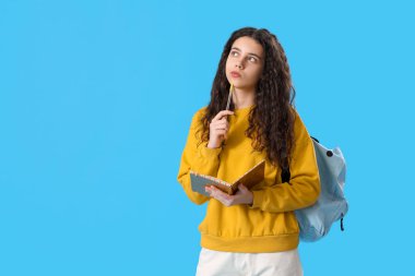 Mavi arka planda not defteri ve sırt çantası olan düşünceli bir bayan öğrenci.