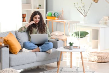Teenage girl using laptop on sofa at home