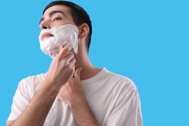 Genç adam açık mavi arka planda tıraş oluyor.