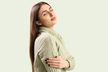 Pretty stylish young woman in warm knitted sweater on mint background