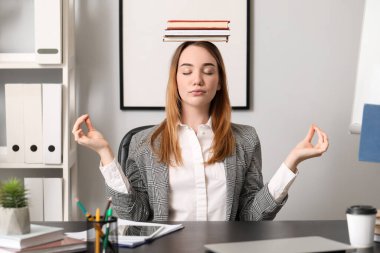 Genç iş kadını ofiste kitaplarla meditasyon yapıyor. Denge kavramı