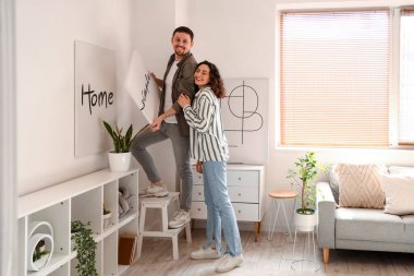 Genç bir çift evdeki ışık duvarına poster asıyor.