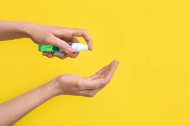 Sarı arka plana dezenfektan süren kadın