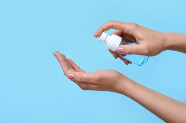 Mavi arka planda dezenfektan kullanan kadın