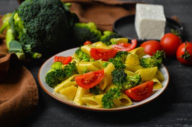 Koyu ahşap arka planda lezzetli makarna ve sebzeli tabak.