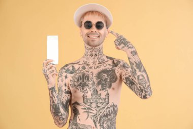 Tattooed man with sunscreen cream on beige background clipart