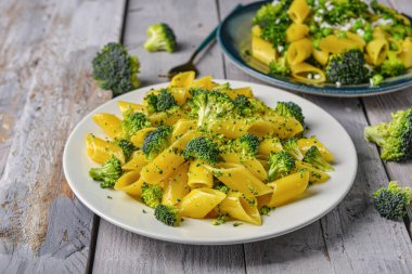 Gri ahşap arka planda lezzetli makarna ve brokoli tabakları.