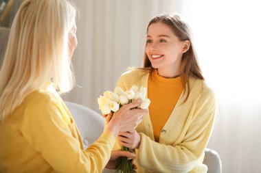 Genç bir kadın evde lalelerle annesini selamlıyor.