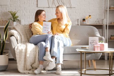 Genç bir kadın evde annesini kartvizitle selamlıyor.