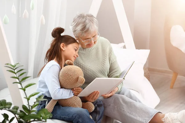 Κοριτσάκι Παιχνίδι Και Γιαγιά Της Διαβάζει Βιβλίο Στην Κρεβατοκάμαρα — Φωτογραφία Αρχείου