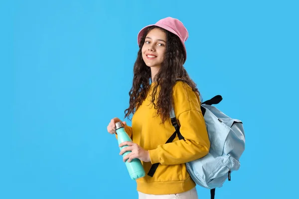Female student with bottle of water and backpack on blue background