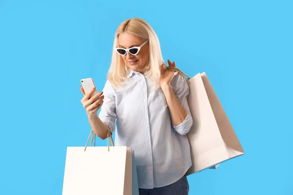 Rijpere Vrouw Met Mobiele Telefoon Boodschappentassen Blauwe Achtergrond — Stockfoto