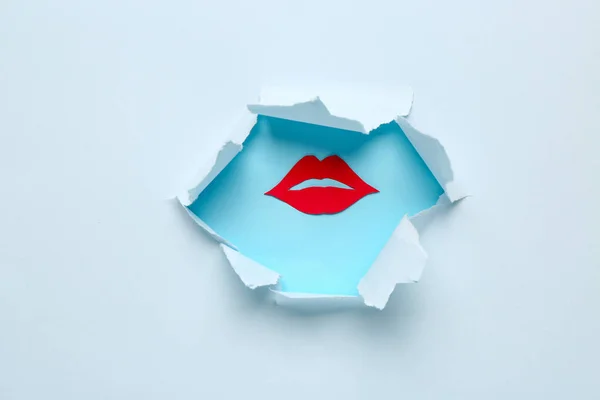 Red paper lips visible through hole in blue paper