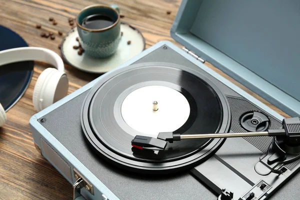 Record player with vinyl disk, headphones and cup of coffee on wooden background, closeup
