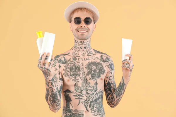 Tattooed man with sunscreen creams on beige background
