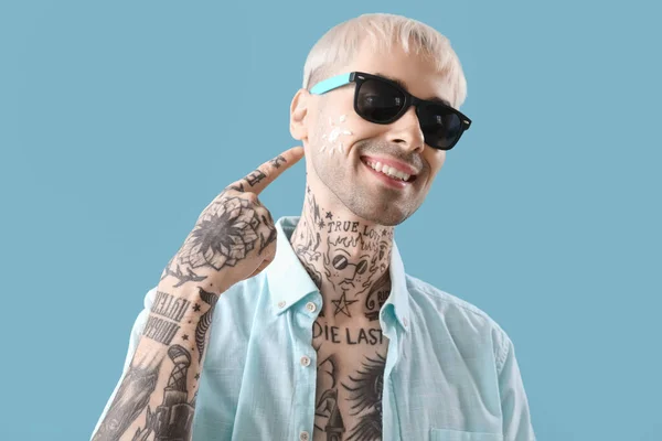 Tattooed man with sunscreen cream on his face against light blue background