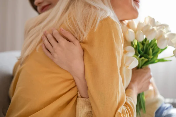 Mature woman with tulips hugging her daughter at home, closeup. Mother\'s Day celebration