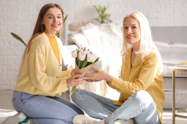 Genç bir kadın, annesini lalelerle ve hediyelerle selamlıyor.