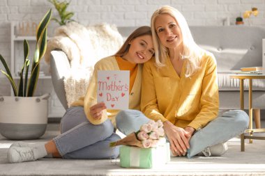 Genç bir kadın evde annesini kartvizitle selamlıyor.