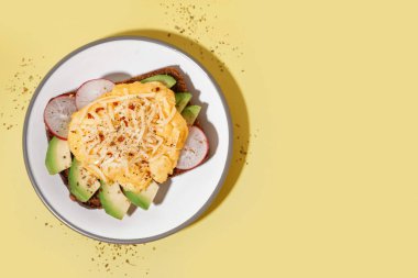 Sarı arka planda lezzetli çırpılmış yumurta, sandviç ve sebze tabağı.