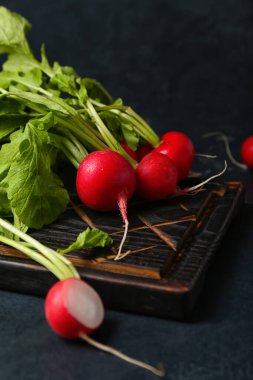 Koyu arkaplanda yeşil yapraklı olgun turp tahtası.