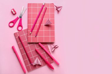 Not defterleri, kırtasiye malzemeleri ve pembe arka planda kağıt uçak kompozisyonu