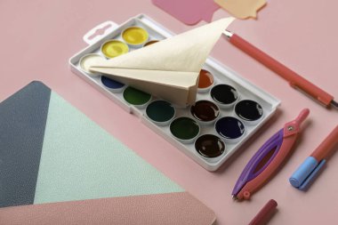 Kırtasiye malzemeleri ve pembe arka planda kağıt uçak kompozisyonu