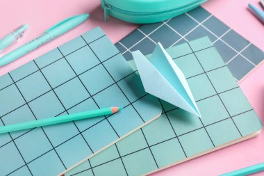 Kırtasiye malzemeleri ve pembe arka planda kağıt uçak kompozisyonu