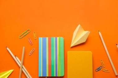 Turuncu arka planda defter, kırtasiye malzemeleri ve kağıt uçak kompozisyonu