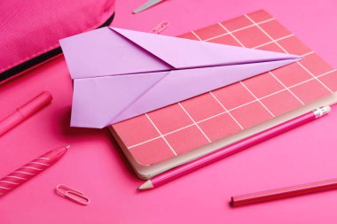 Kırtasiye malzemeleri ve pembe arka planda kağıt uçak kompozisyonu