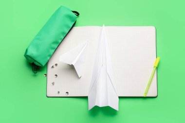 Kırtasiye malzemeleri ve yeşil arka planda kağıt uçaklar ile kompozisyon