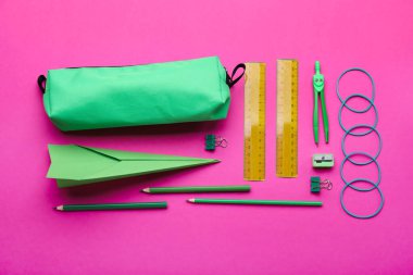 Kırtasiye malzemeleri ve pembe arka planda kağıt uçak kompozisyonu