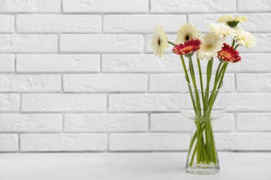 Beyaz tuğla duvarın yanındaki masada Gerbera çiçekleri olan vazo.