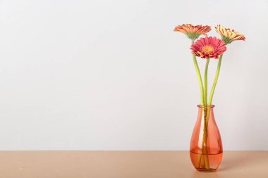 Işık duvarının yanındaki masada Gerbera çiçekleri olan vazo.