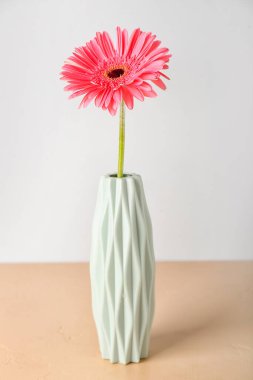Işık duvarının yanındaki masada Gerbera çiçekli vazo.