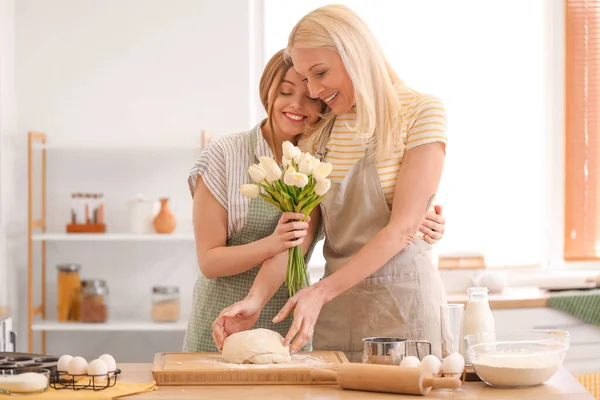 Genç bir kadın mutfakta lalelerle annesini selamlıyor.