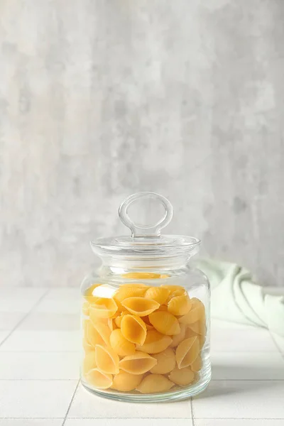 Jar with raw conchiglie pasta on table